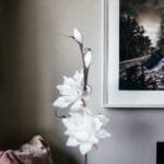 Weiße Kunstblumen neben gerahmtem Bild an der Wand.