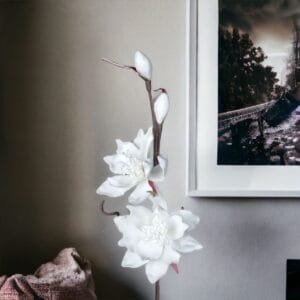 Weiße Kunstblumen neben gerahmtem Bild an der Wand.