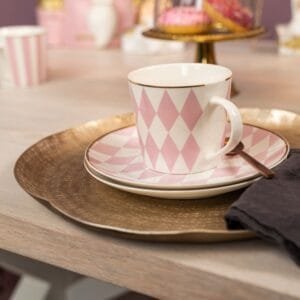 Tasse mit rosa Rautenmuster auf Teller, Holztisch im Hintergrund.