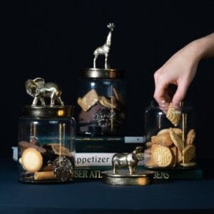 Hand greift nach Keksen in dekorativen Gläsern mit Tierfiguren.